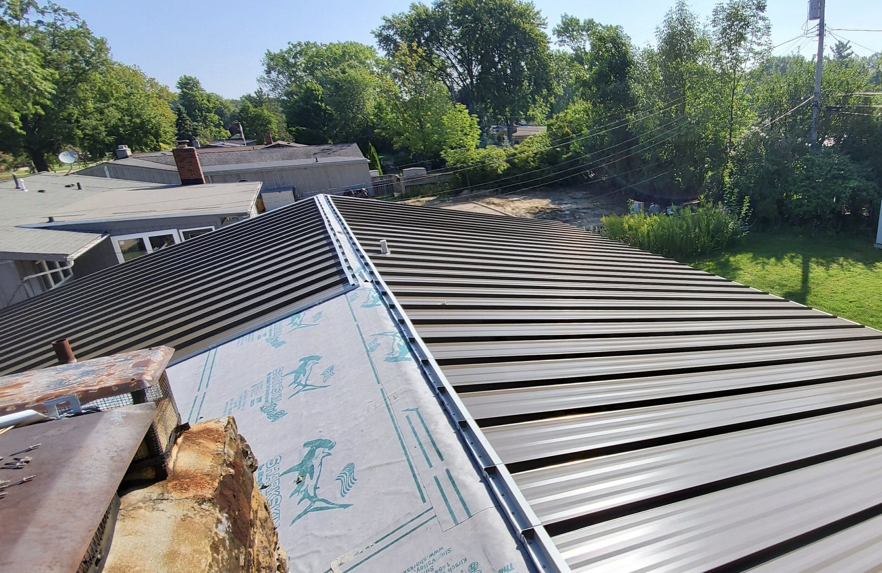 Standing-seam metal roof installation in Plant City with underlayment still exposed at the chimney