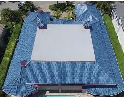 Aerial of a blue shingle roof with a large white low-slope membrane in the center and two turret roofs